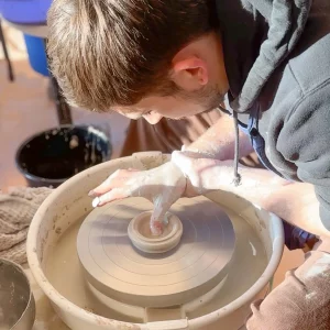 Un homme travaillant l'argile au tour de potier, en train de compresser la base de son pot à l'Atelier Studio Alchimies à Mauraz, Vaud.